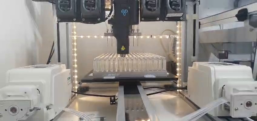 The PleniDose Gantry filling a loaded cartridge holder at Panacea Bio Chem — the eight-cannula head, the pumps above it and the holder below, photographed on the bench
